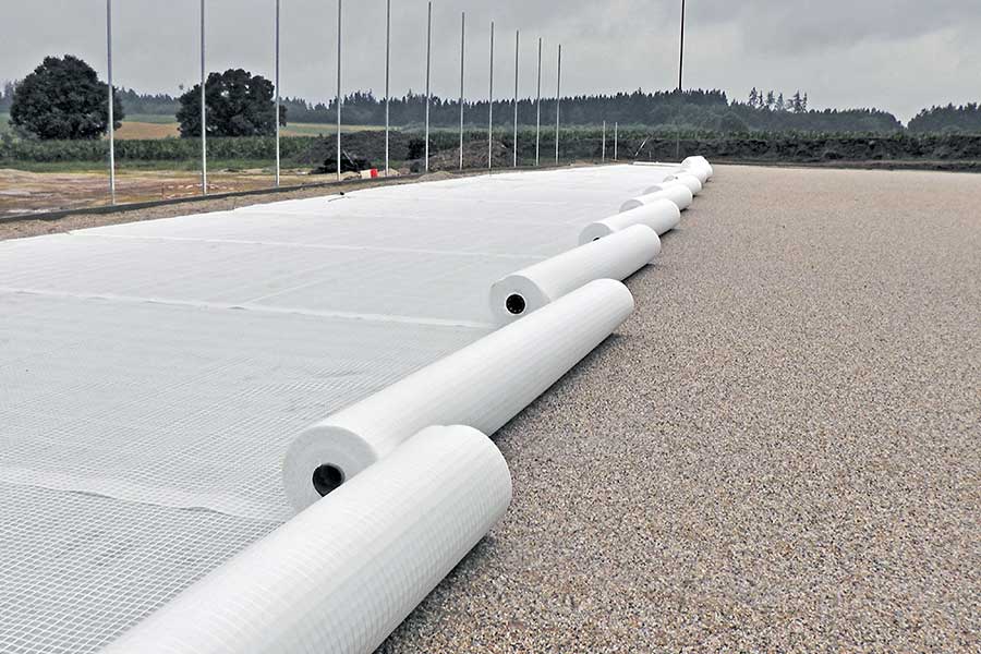 Step 1 in the construction of the artificial turf pitch: Roll out the GEOGITTER onto the split bedding.